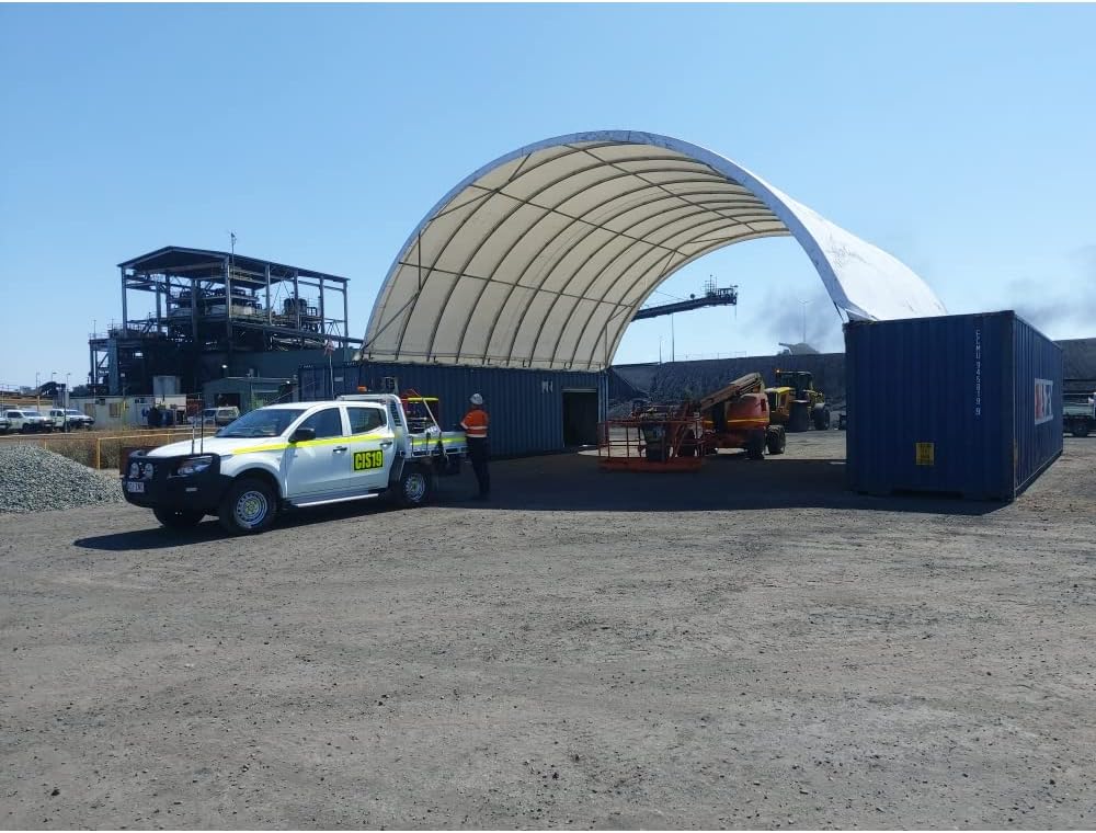 Large shipping container canopy shelter at industrial site spanning two blue containers