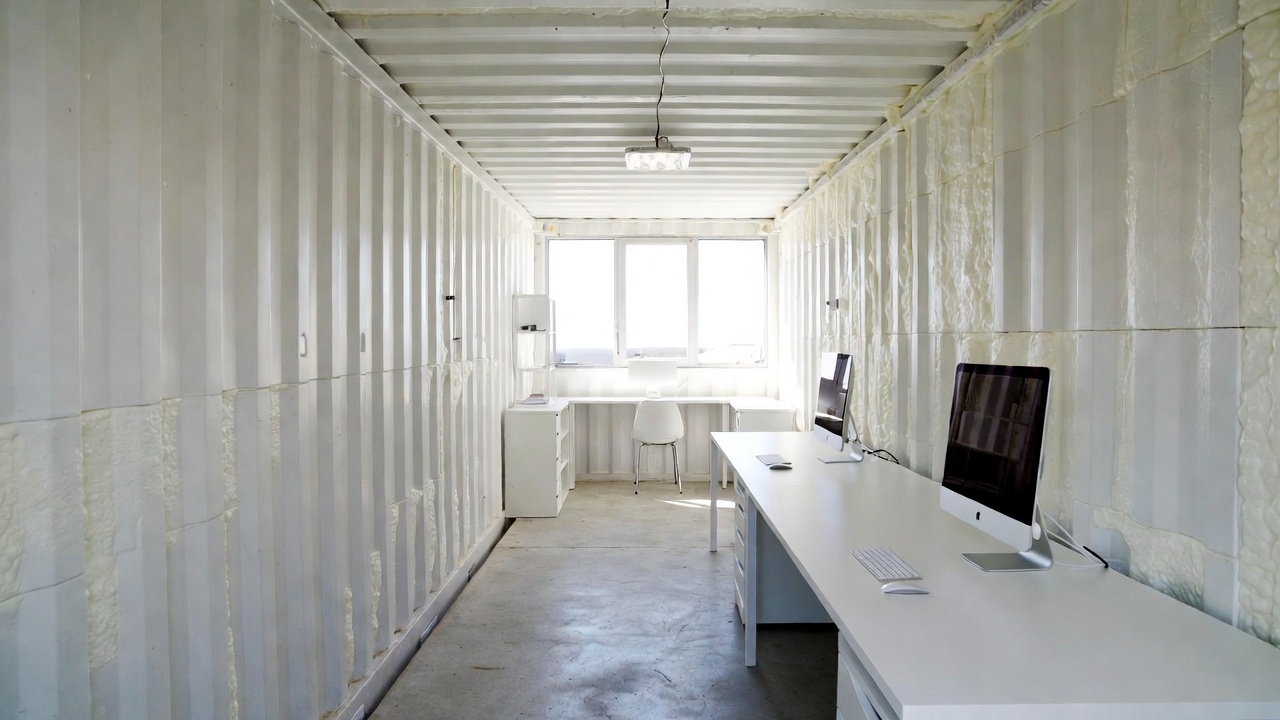 Container office interior with white walls, desk and iMac computers